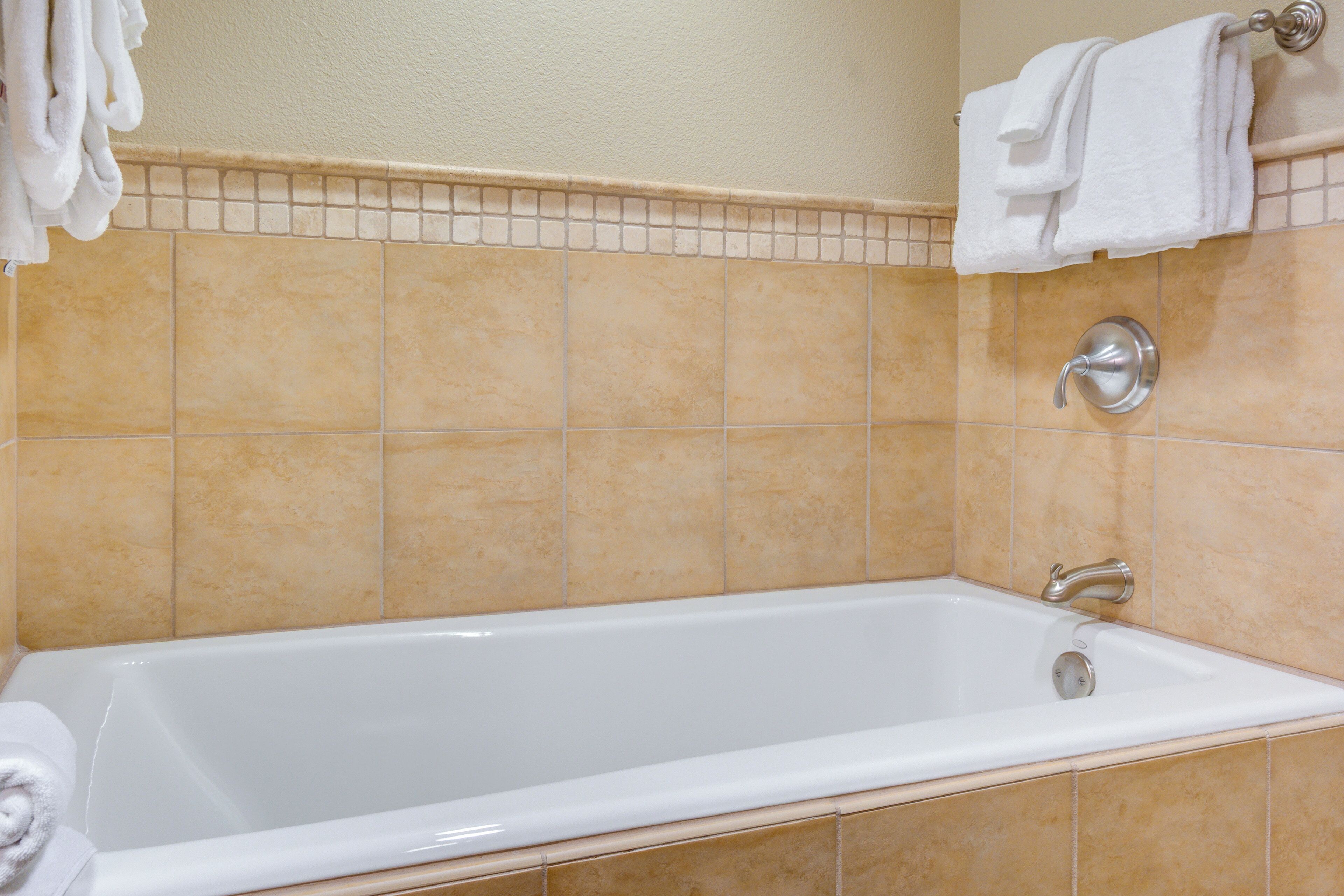 A bathroom with a white bathtub, beige tiles, and a towel rack with white towels.