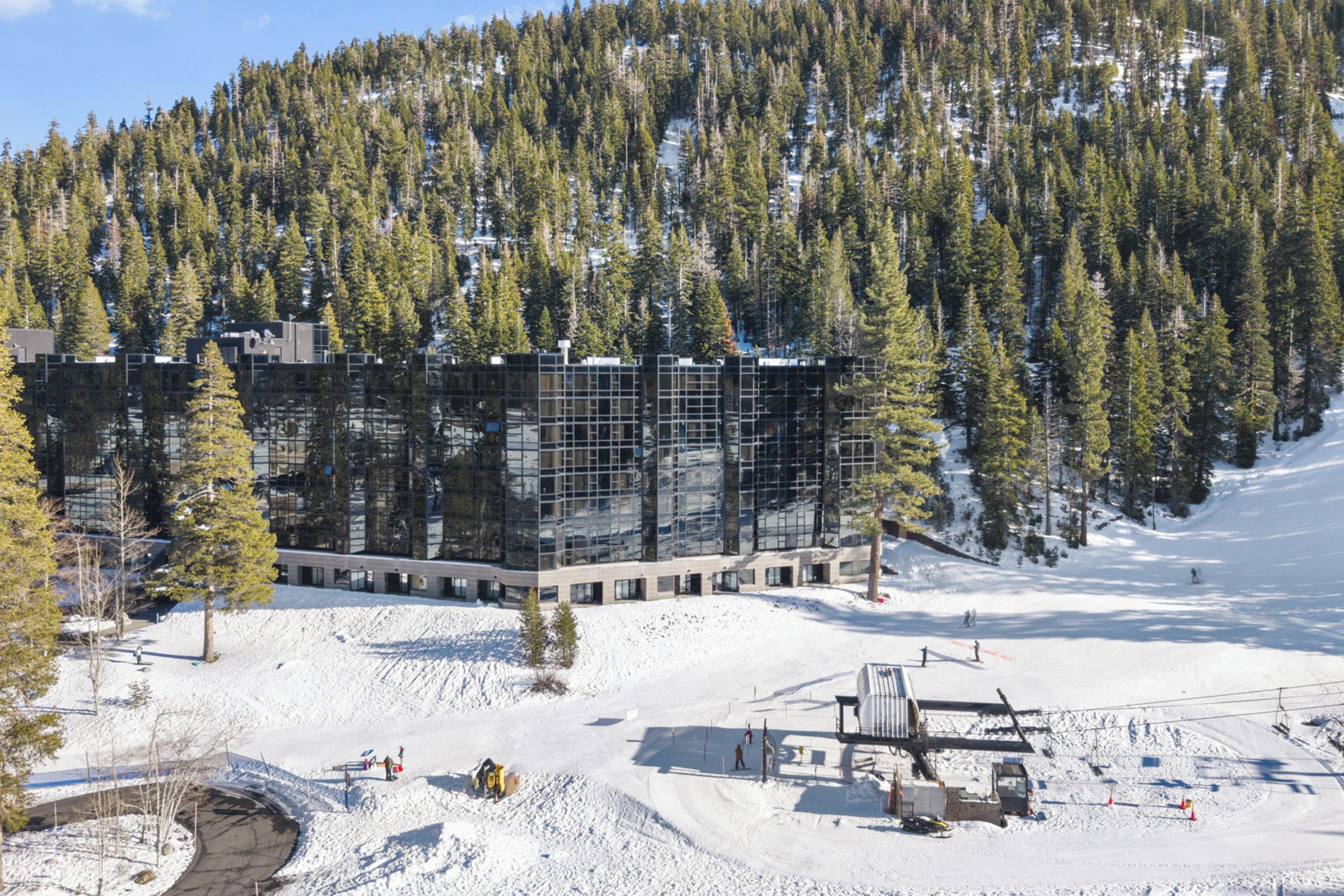 A modern building with a glass facade surrounded by snow-covered terrain and dense forest.