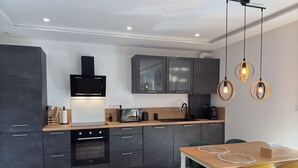 A modern kitchen with dark cabinets, a built-in oven, and a microwave. There is a wooden dining table with yellow chairs and a white tablecloth. - Jacuzzi, Sauna, Private - Escape at your fingertips (Aspach-le-Bas)