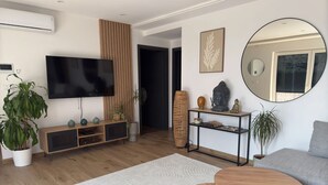A modern living room with a flat-screen TV, wooden flooring, a grey sofa, a round coffee table, and a large mirror. - Jacuzzi, Sauna, Private - Escape at your fingertips (Aspach-le-Bas)