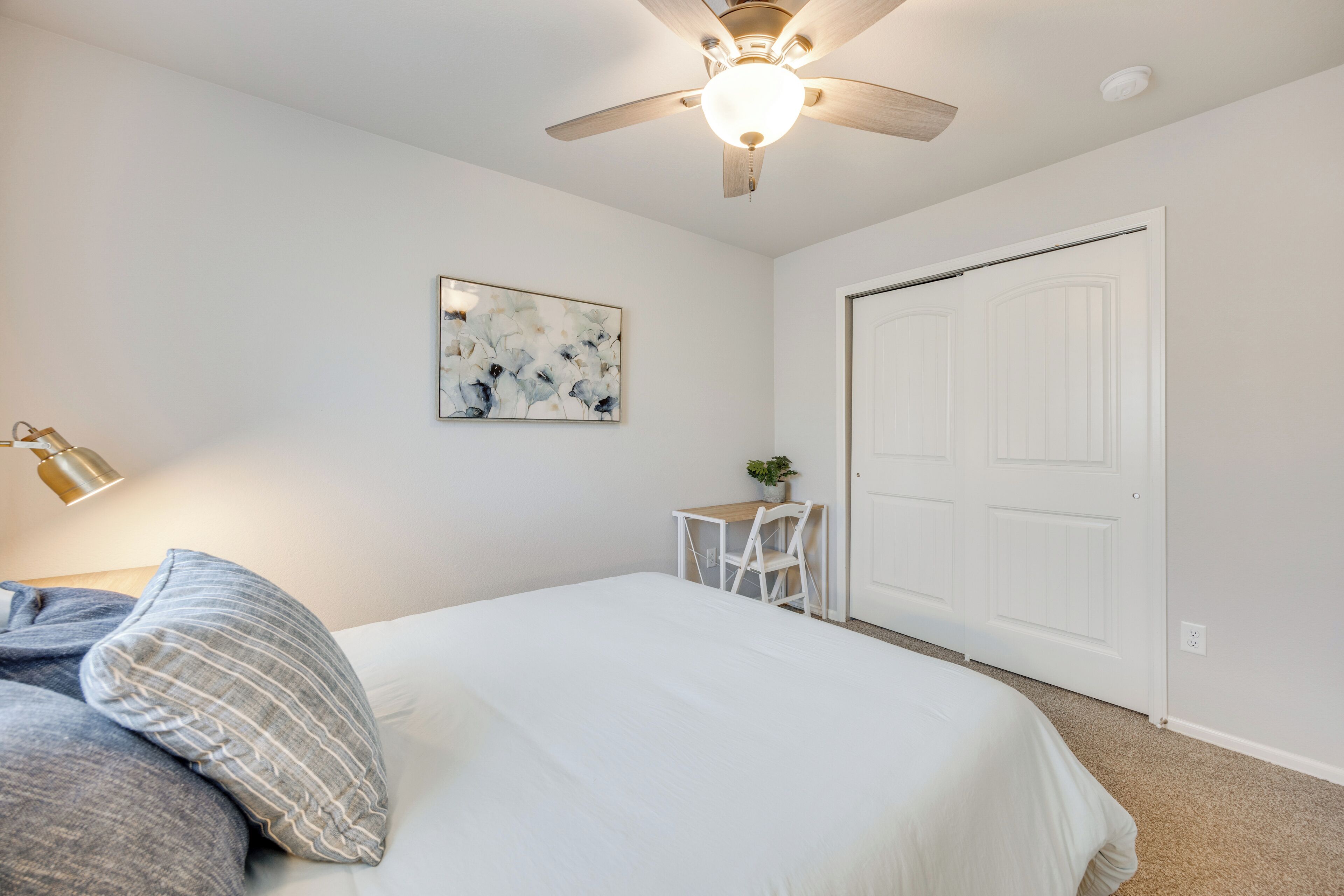 A bedroom with a bed, a desk, a chair, a ceiling fan, and a door.