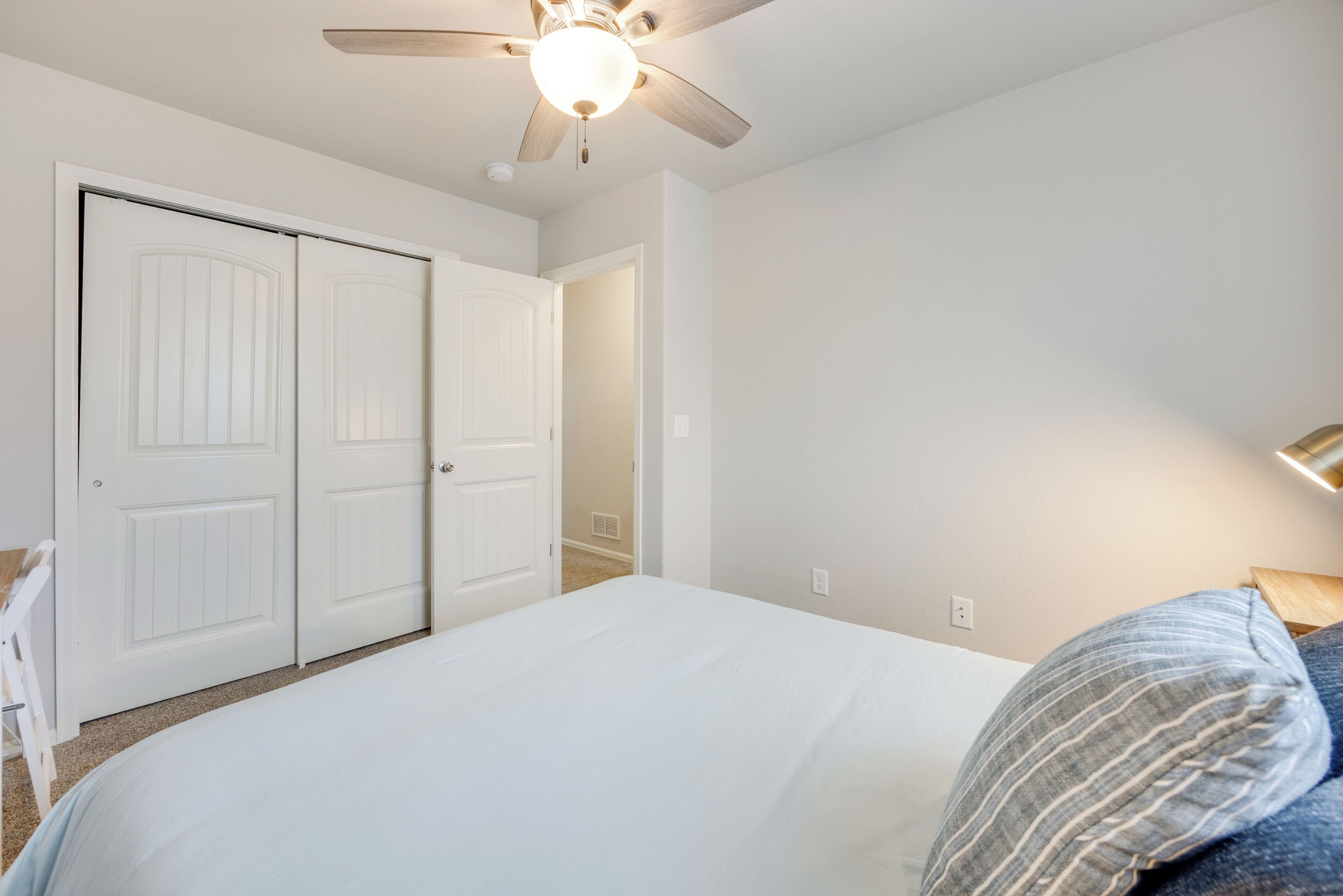 A bedroom with a bed, a ceiling fan, and a door.