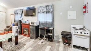 A compact living space with a kitchenette, a flat-screen TV, a microwave, a stove, and a small trash bin. - 8 Mi to Dtwn Cle: Cozy Couple's Retreat w/ Gym! (Cleveland)