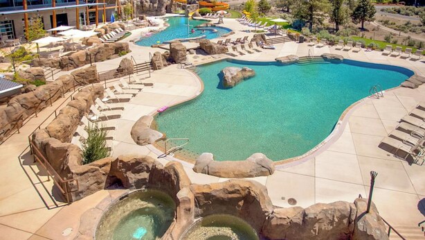 Ein Resort mit mehreren Pools, darunter ein großer Mittelpool und kleinere Whirlpools, umgeben von Liegebereichen und natürlichen Felsformationen.