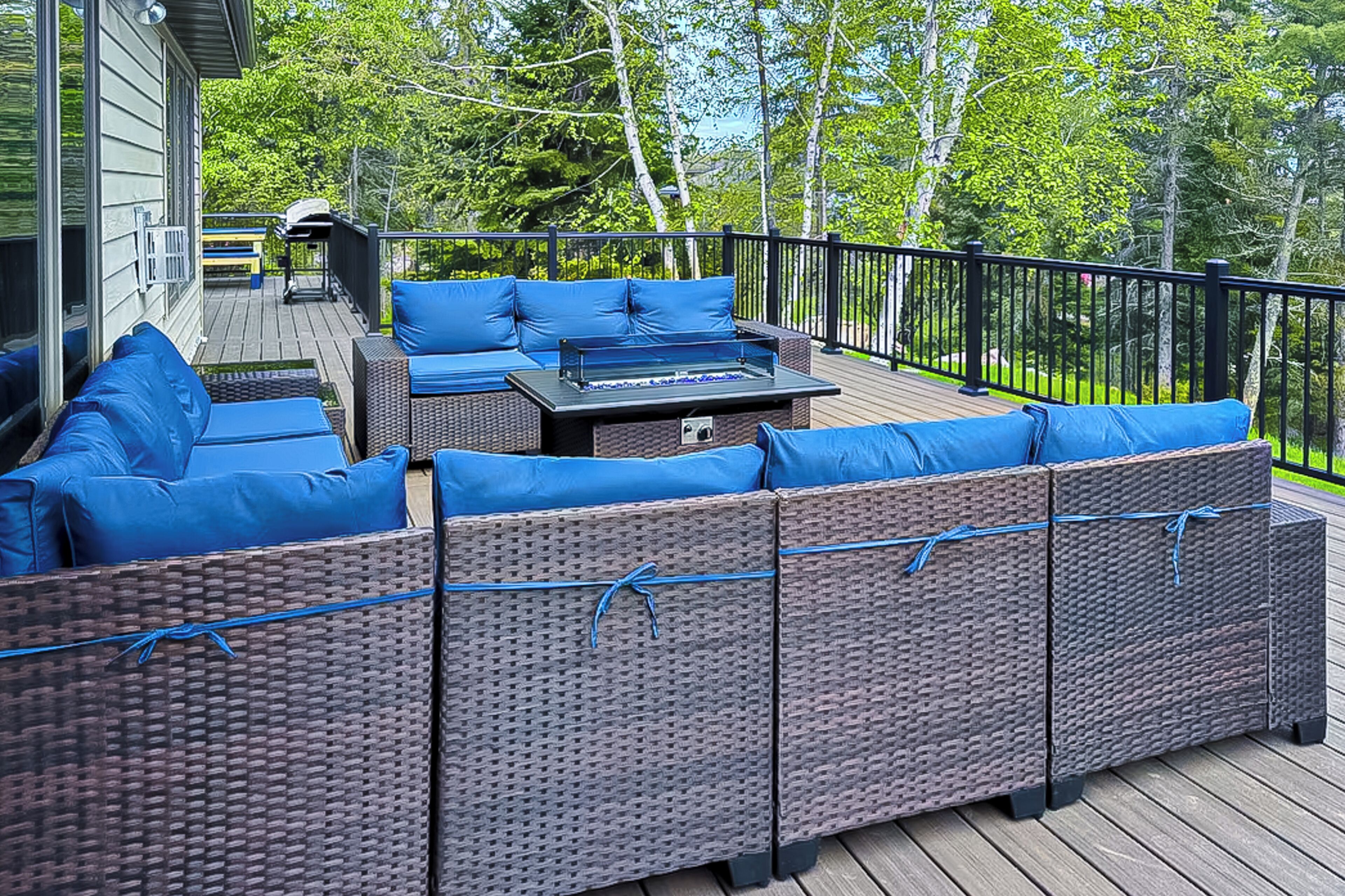 A deck with wicker furniture and blue cushions, a barbecue grill, and a view of trees.