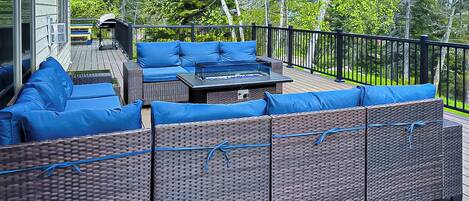 A deck with wicker furniture and blue cushions, a barbecue grill, and a view of trees.