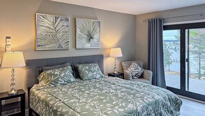 A bedroom with a large bed, two wall-mounted lamps, a chair, and a view of the outdoors. - Luxury Rainy Lake House With Private Dock! (International Falls)