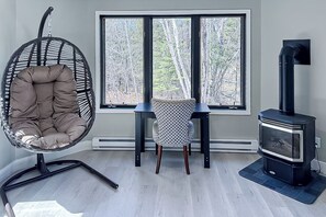 A room with a large window, a hanging chair, a patterned chair, and a wood-burning stove. - Luxury Rainy Lake House With Private Dock! (International Falls)