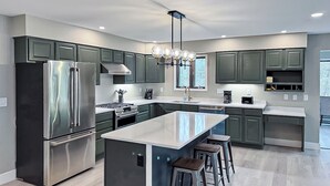 A modern kitchen with a large island, stainless steel appliances, and green cabinetry. - Luxury Rainy Lake House With Private Dock! (International Falls)