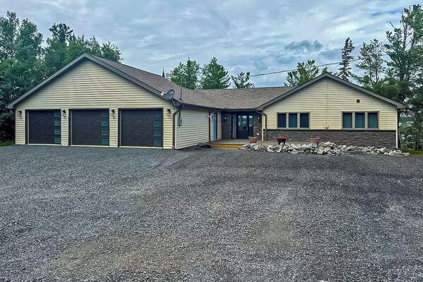 A two-story house with a gravel driveway and a stone wall. - Luxury Rainy Lake House With Private Dock! (International Falls)