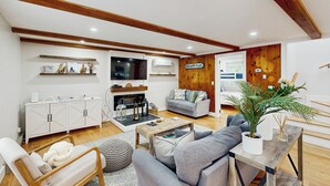 A modern living room with a fireplace, grey sofas, wooden beams, and a television. - Marthas Vineyard Vacation Retreat - Relax! (Vineyard Haven)
