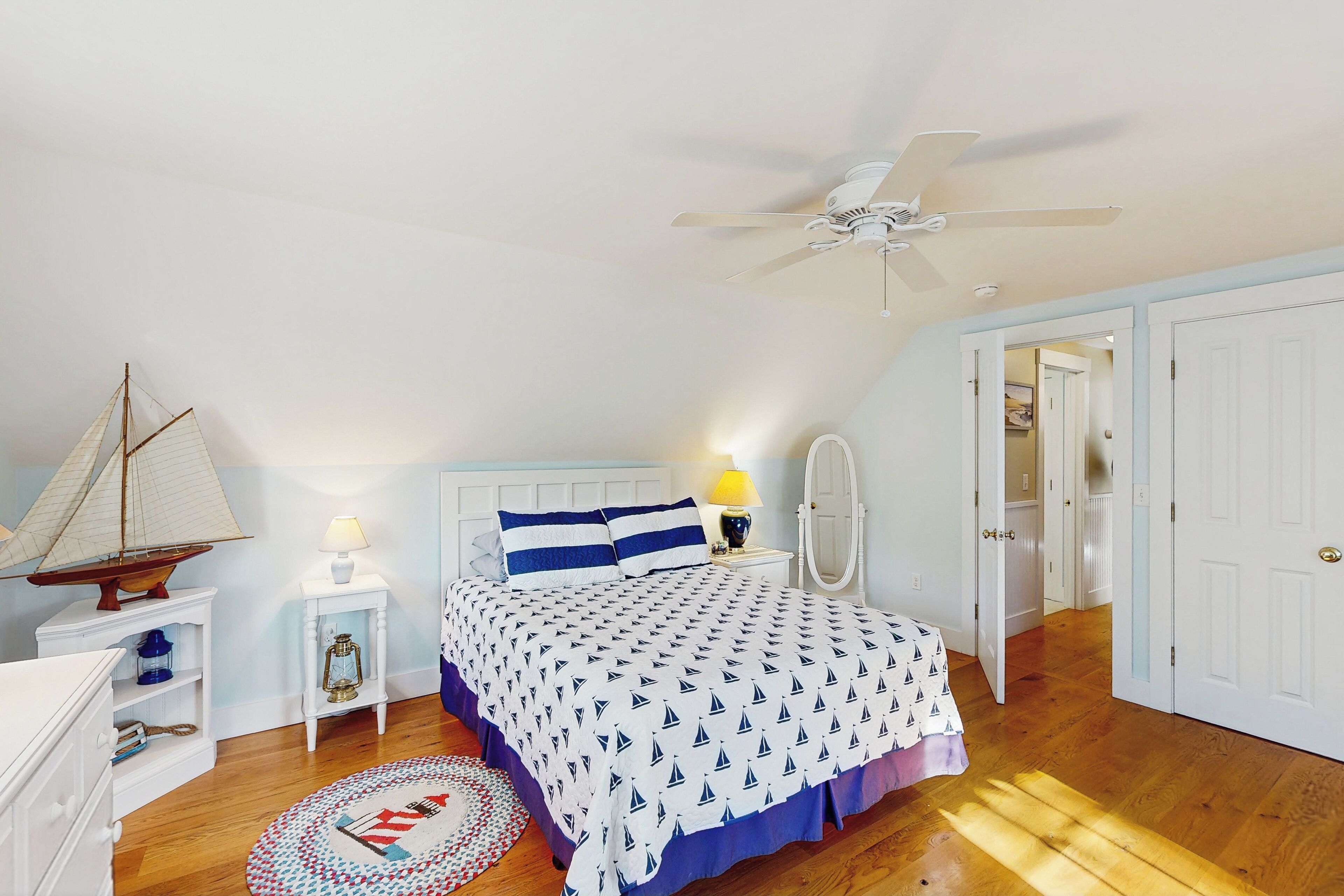 Ein Schlafzimmer mit einem Bett, einem Deckenventilator, einem Nachttisch mit Lampe, einem Schiffsmodell und einem runden Teppich.