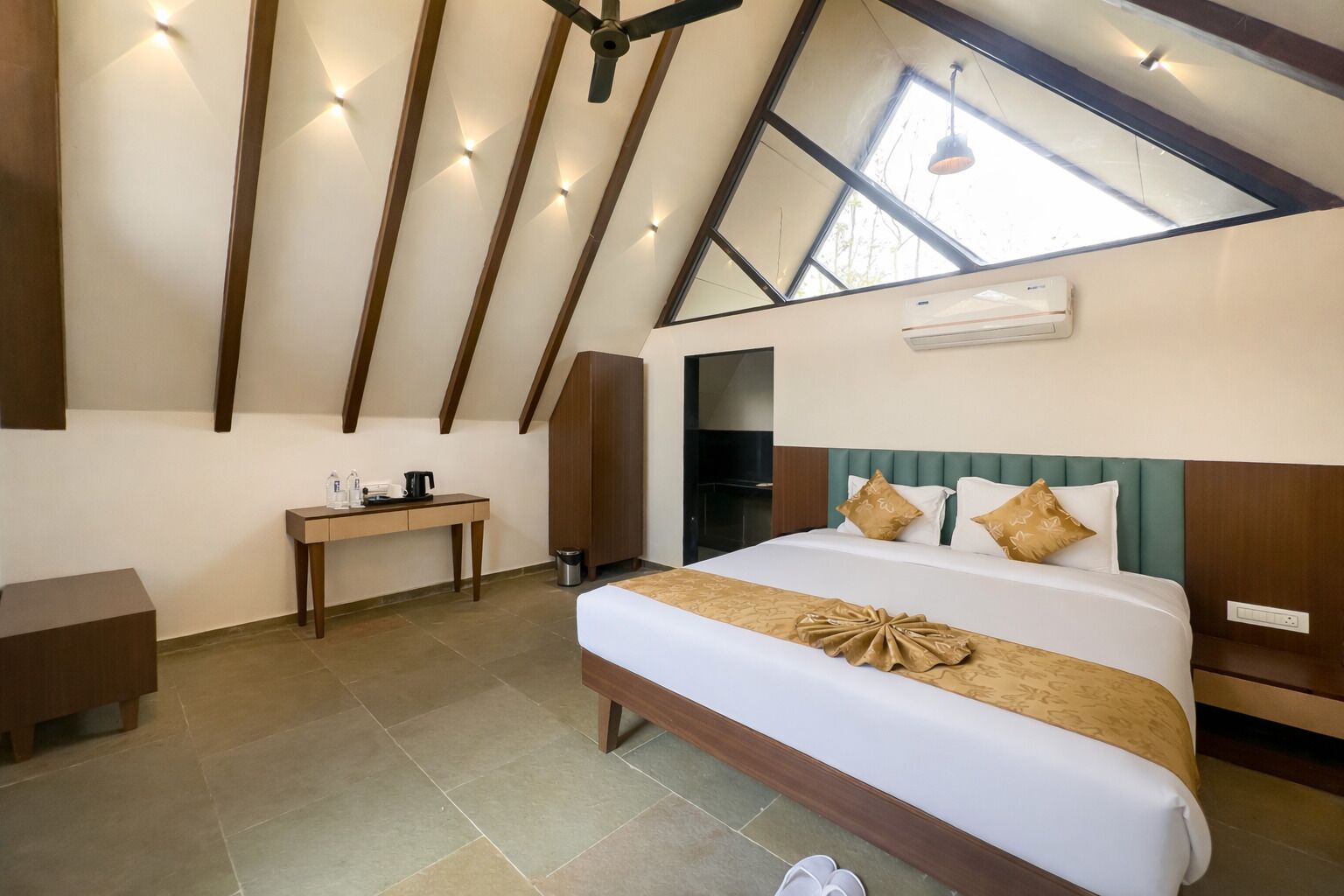Een slaapkamer met een schuine kap, een bed met een decoratieve hoofdbord, een nachtkastje, een bureau en een kledingkast.