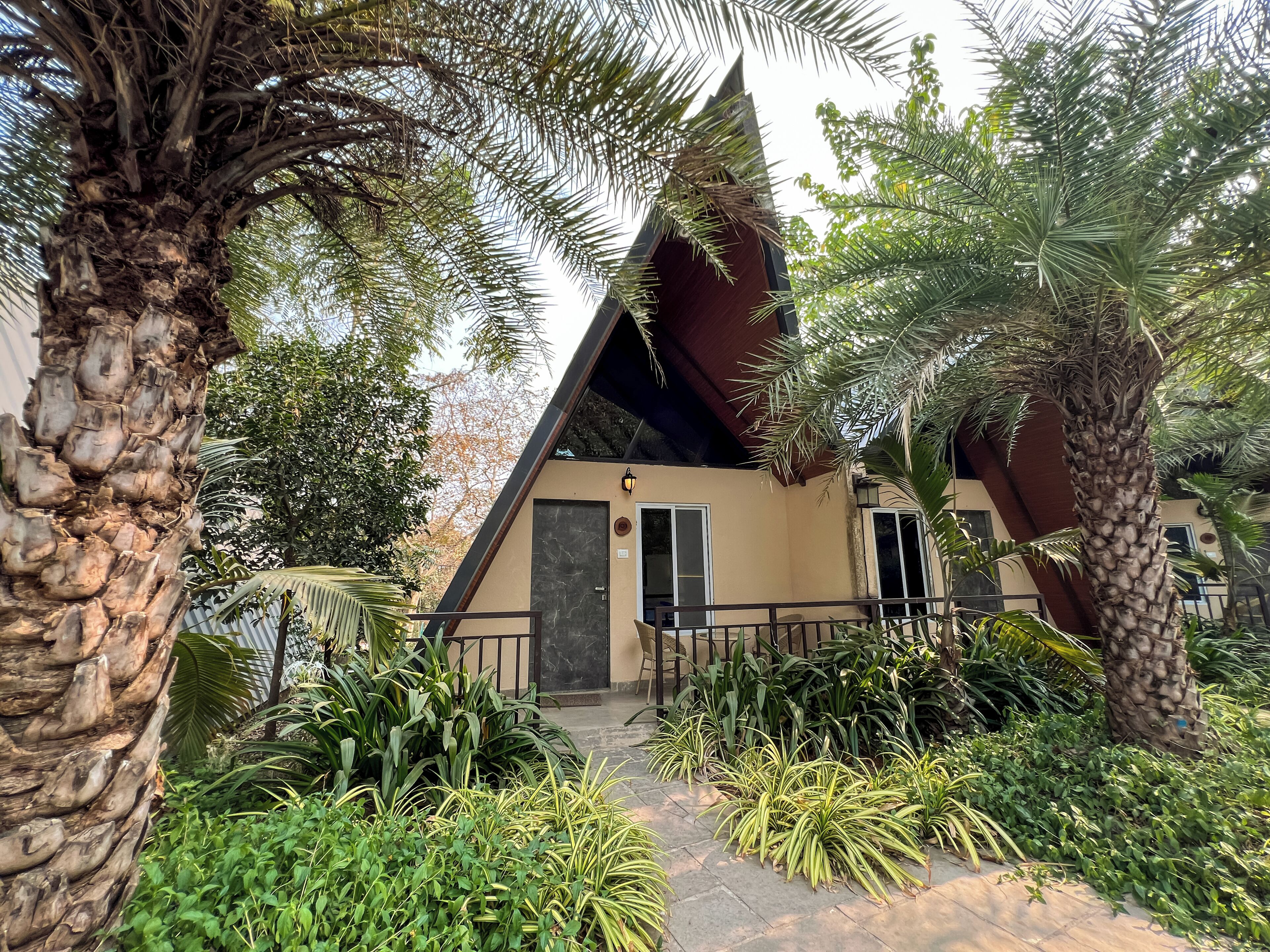 A building with a triangular roof, surrounded by lush greenery and palm trees.