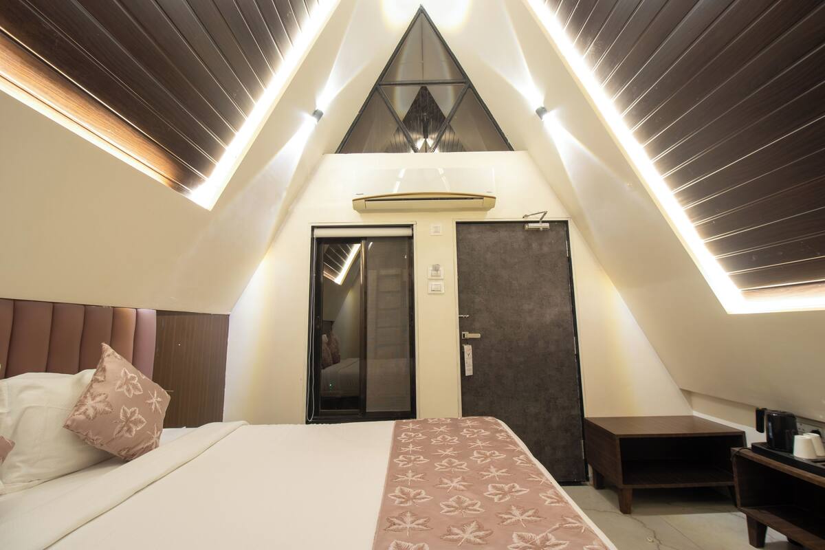 Ein modernes Hotelzimmer mit schrägen Wänden, einem Bett mit gemusterten Bettwäsche, einem Nachttisch und einer kleinen Arbeitsfläche.