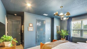 Quarto com cama, escrivaninha, cadeira, planta em vaso e janela com cortinas.