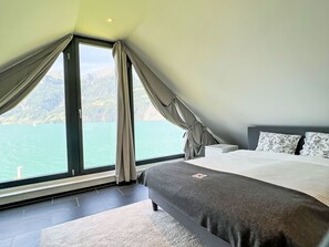 A bedroom with a large window, a bed, and a view of a body of water and mountains. - Villa am See 5 / Beach House by Interhome (Sisikon)
