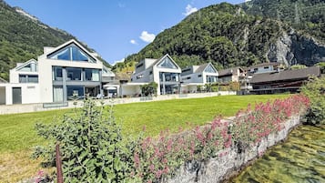 A modern residential area with houses, a clear stream, and a mountainous backdrop.