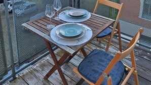 Una terraza de madera con una mesa preparada para dos, con vista a una zona residencial con árboles y edificios.