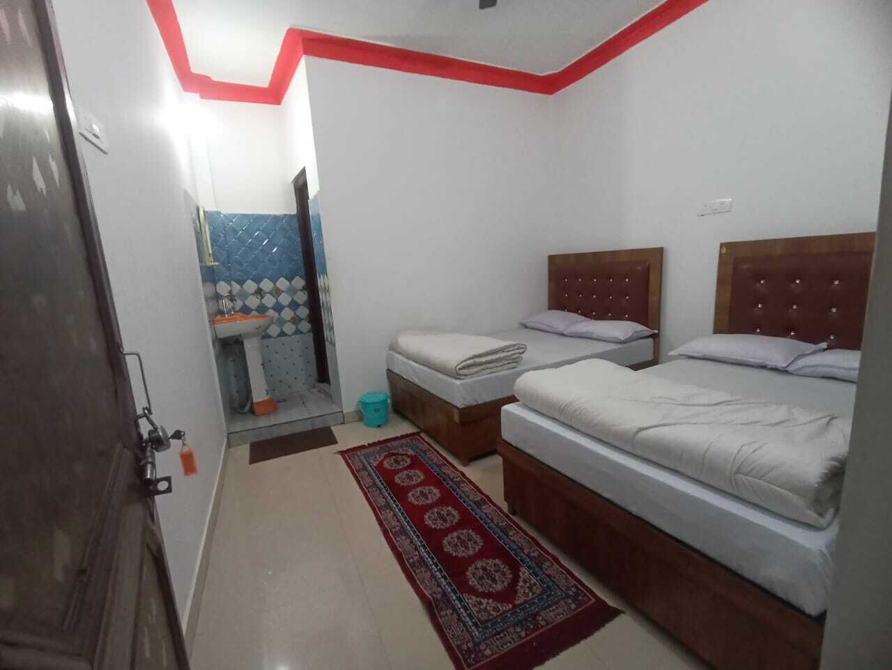 Un dormitorio con dos camas, un baño pequeño y una pared de acento roja.