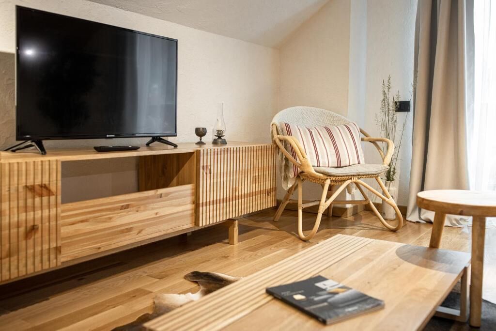 Una sala moderna con un televisor de pantalla plana sobre un mueble de madera, un sillón de mimbre con cojín a rayas y una mesa de centro de madera.