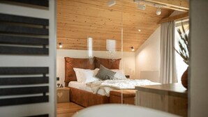 Una camera da letto con soffitto in legno, un letto con biancheria bianca e un comodino con una lampada.