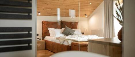A bedroom with a wooden ceiling, a bed with white bedding, and a nightstand with a lamp.