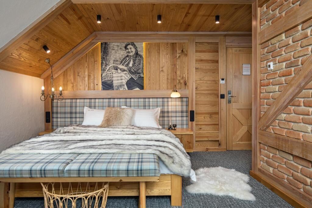 Ein gemütliches Schlafzimmer mit Holzboden, einer Karo-Bettdecke und einem großen Fenster mit Blick ins Freie.