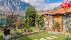 Une maison avec une façade en pierre, une porte en bois et un jardin agrémenté de plantes en pot et d’une montgolfière.