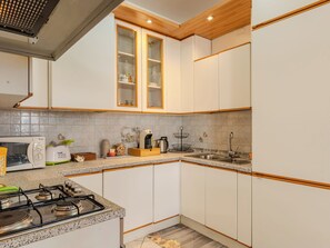 Una cocina con armarios blancos, encimera de granito, estufa a gas, cafetera y un lavamanos.