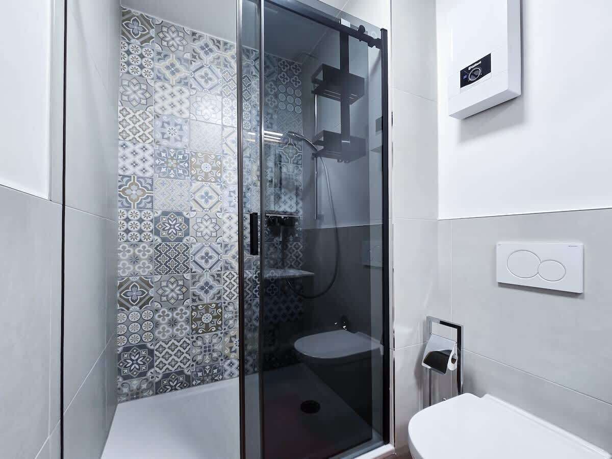 Ein modernes Badezimmer mit einer gläsernen Dusche, einem Musterfliesenbelag, einer Toilette und einem wandmontierten Wasserhahn.