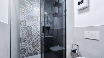Ein modernes Badezimmer mit einer gläsernen Dusche, einem Musterfliesenbelag, einer Toilette und einem wandmontierten Wasserhahn.