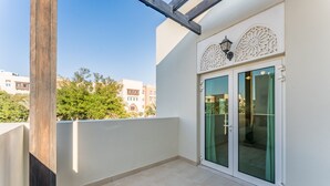 Ein Balkon mit einem hölzernen Pfosten, einer Glastür mit grünem Vorhang und einer weißen Wand mit dekorativer Beleuchtung.