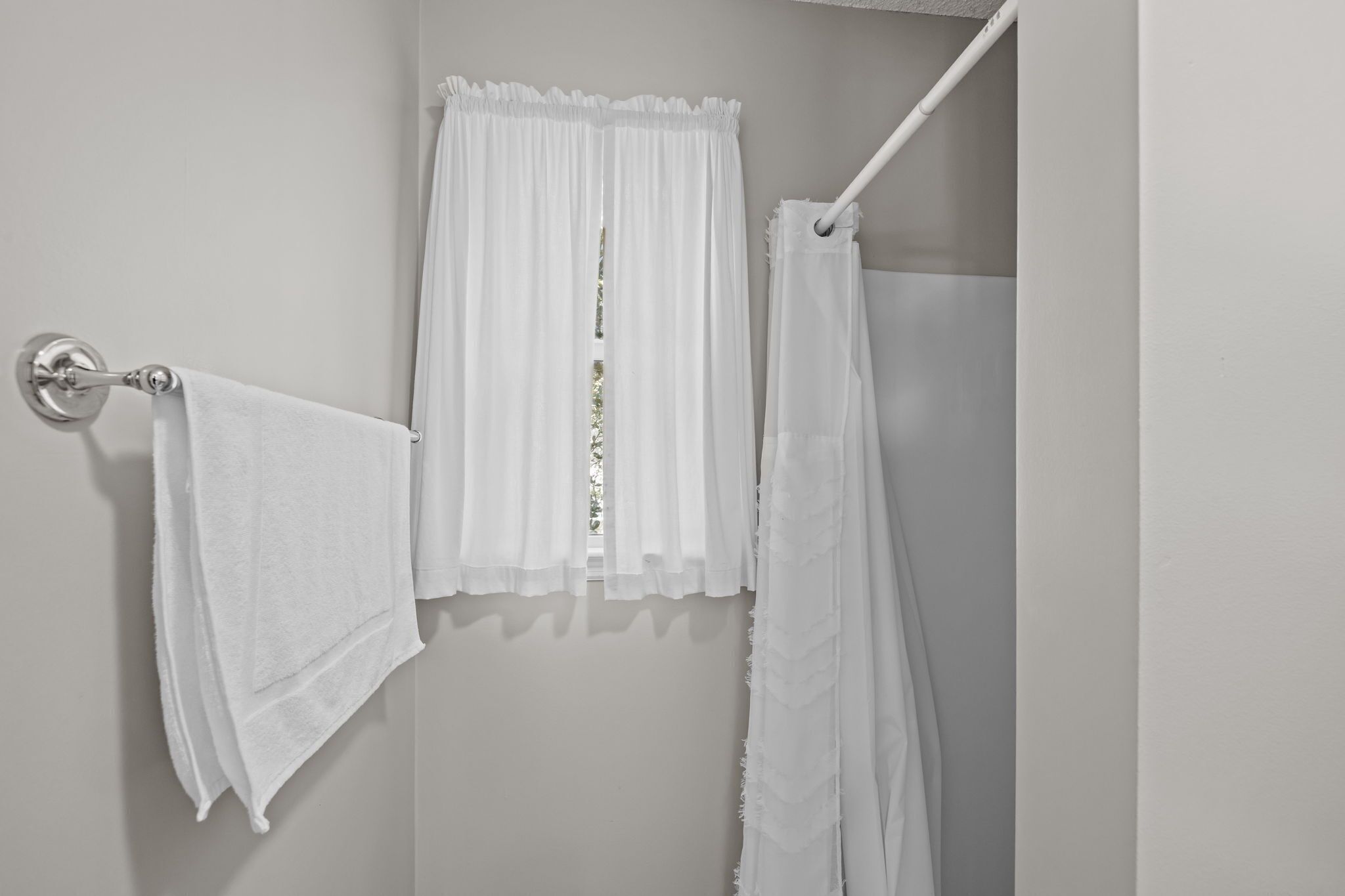 A bathroom with white towels hanging on a rack, a white shower curtain, and a white towel on a hook.