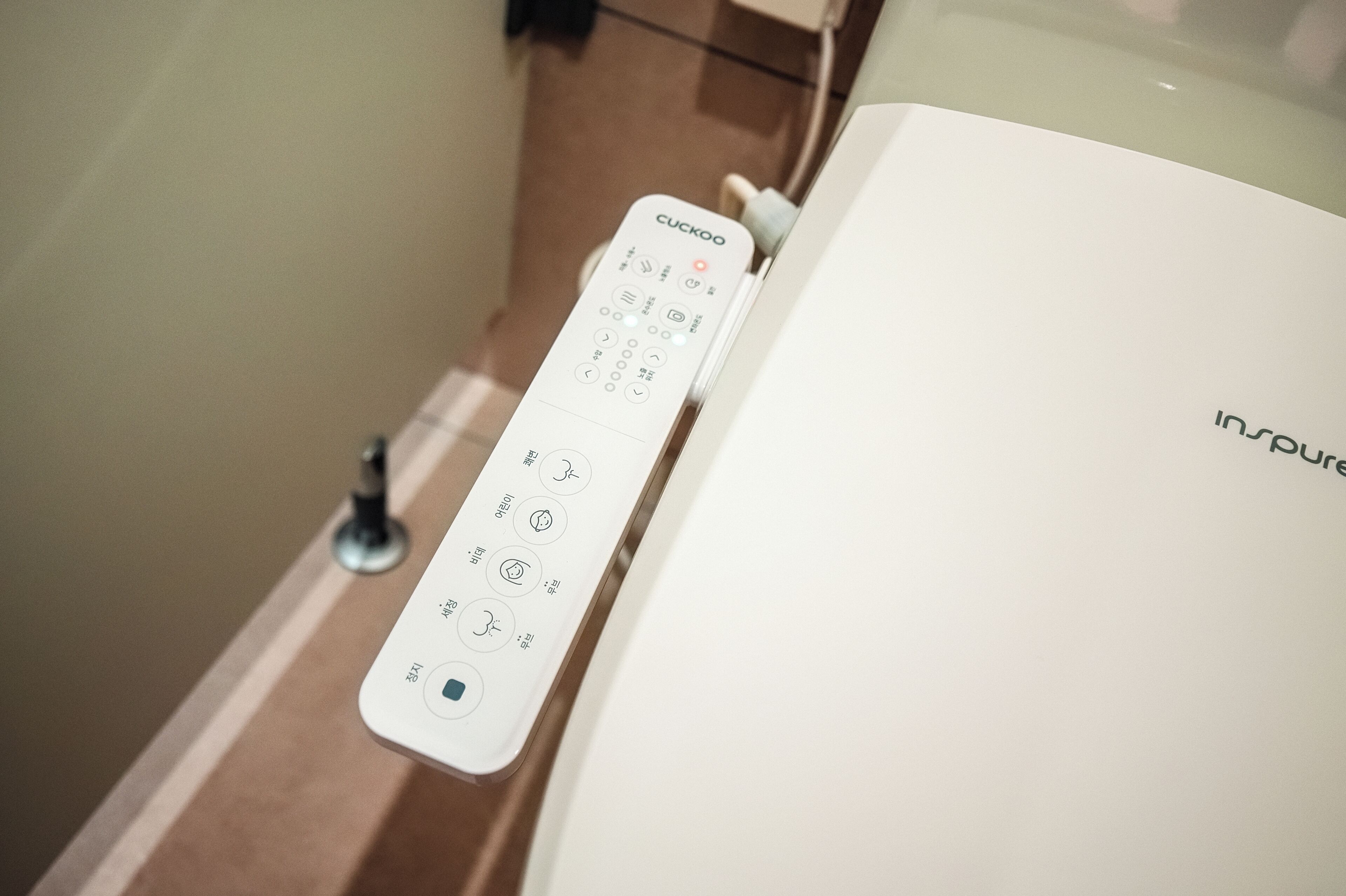 A white remote control with multiple buttons and icons, placed on a surface next to a white object with the word "inspire" visible.