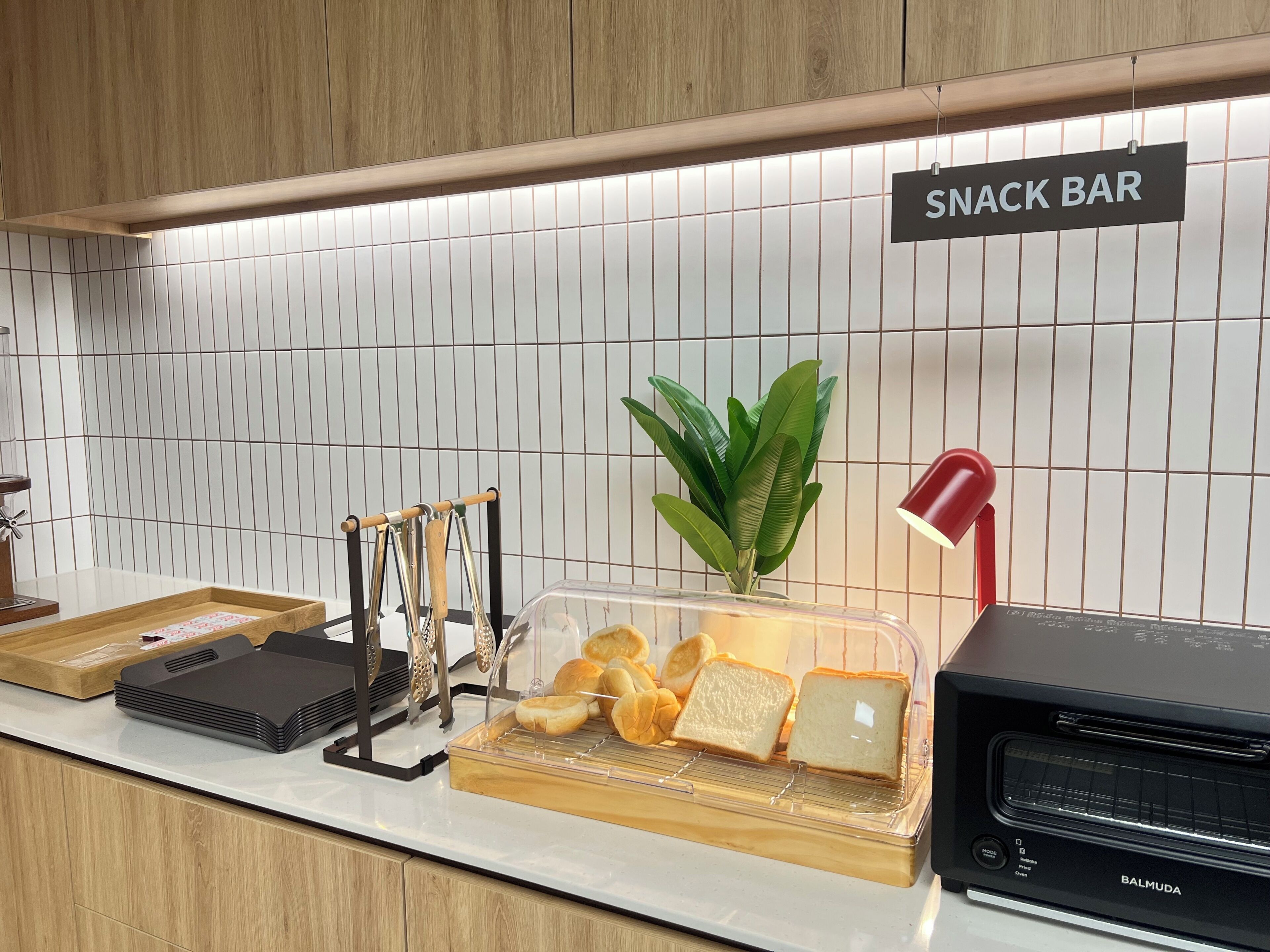 Angolo con snack bar, insegna, pianta, esposizione di pane, lampada rossa e forno Barmuda.