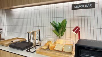 Angolo con snack bar, insegna, pianta, esposizione di pane, lampada rossa e forno Barmuda.