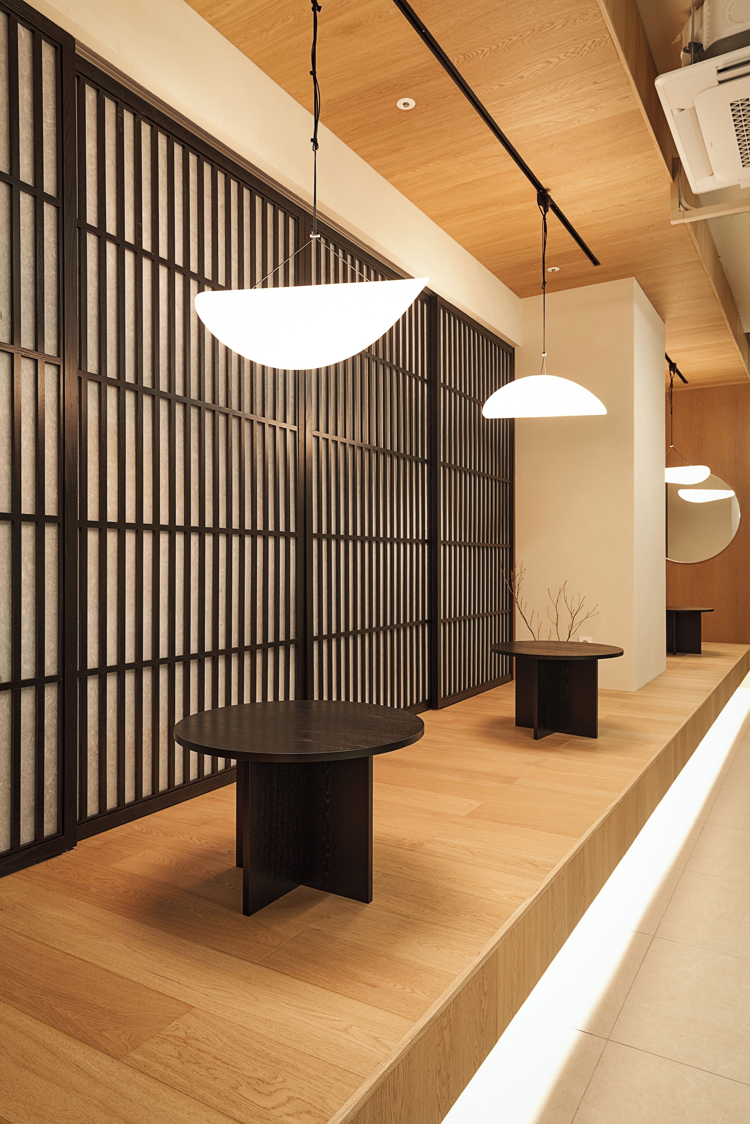 A modern interior with a wooden reception desk, black pendant lights, and a wooden slat partition.