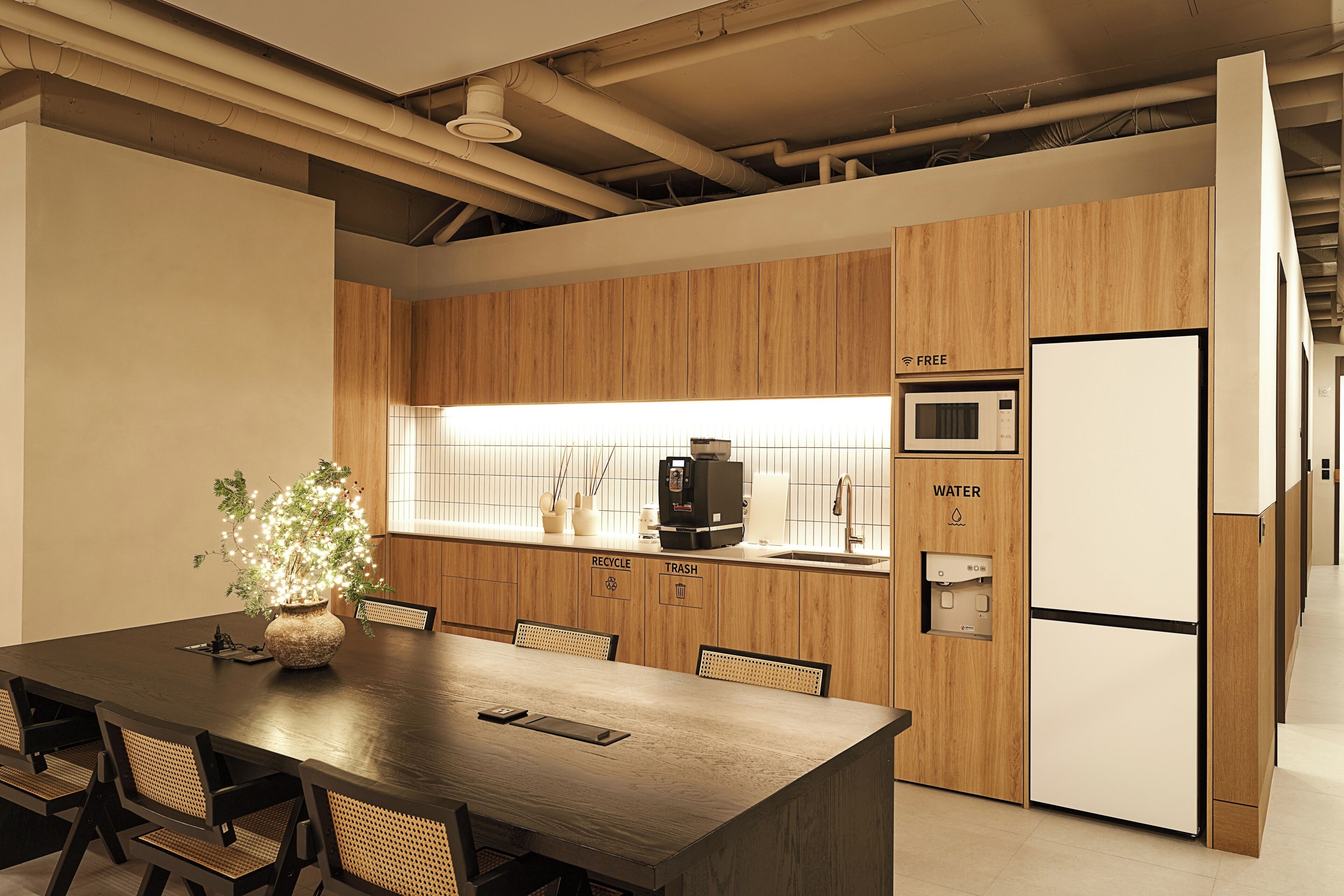 A modern kitchen with a wooden countertop, a microwave, a water dispenser, and a trash bin.