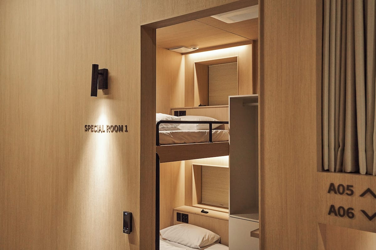A bunk bed room with a small desk and a window with blinds.
