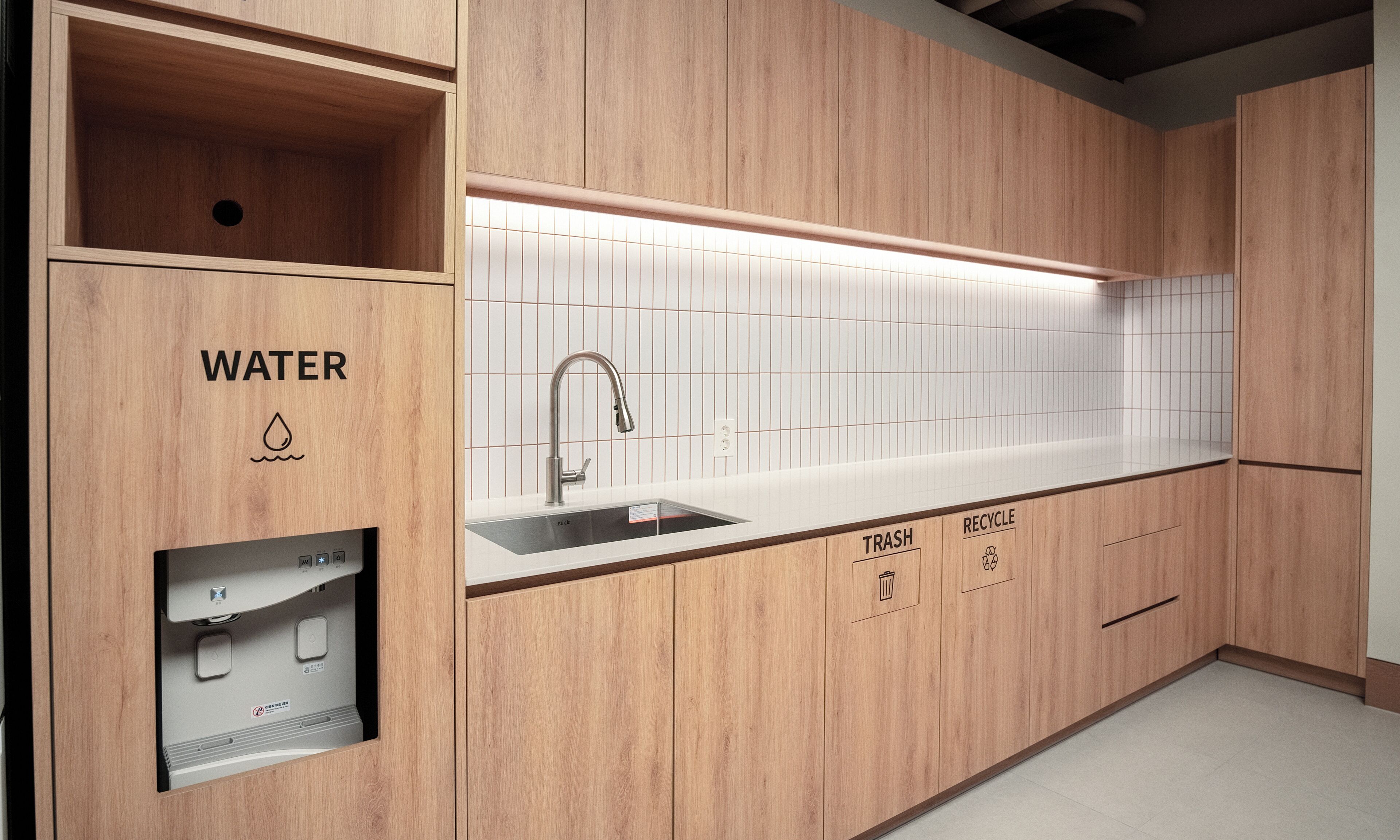 A modern kitchen with wooden cabinetry, a built-in sink, and a water dispenser.