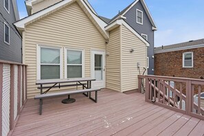 A wooden deck with a picnic table, a white door, and a brick wall. - Sea Bright Gem Steps To Beach + Parking 4 Bedroom Home (Rumson)
