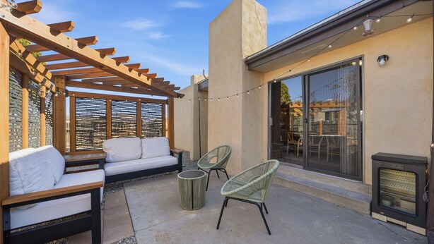An outdoor patio with a wooden pergola, white cushioned seating, wicker chairs, and a small round table. - Albuquerque Escape Hot Tub + Atrium 4 Bedroom Home (Albuquerque)