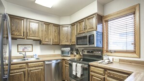 A kitchen with wooden cabinets, stainless steel appliances, and a window with blinds. - H5 Meadow Creek 3 Bedroom Townhouse (Vail)