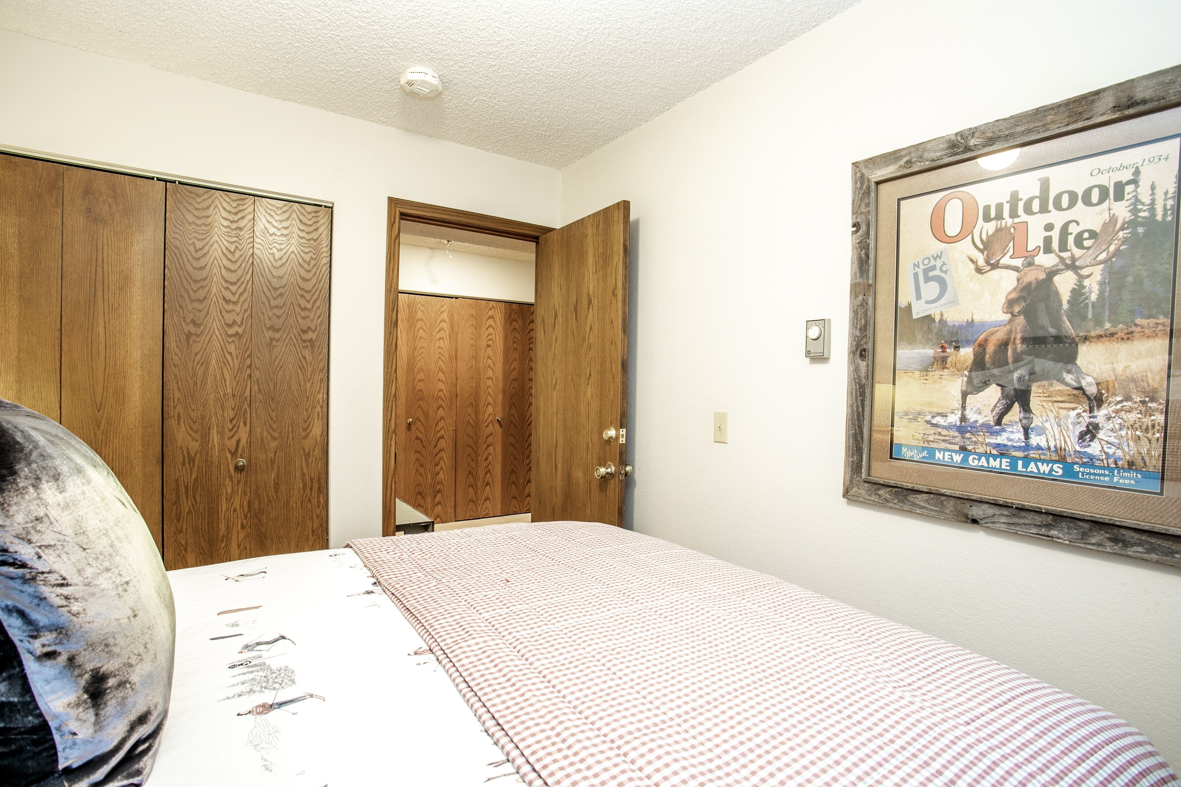 A bedroom with a bed, a wooden wardrobe, and a framed magazine on the wall.
