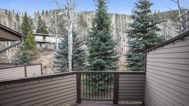 A wooden deck with a metal railing, surrounded by trees and a mountainous backdrop. - H5 Meadow Creek 3 Bedroom Townhouse (Vail)