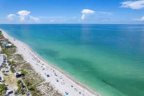 An aerial view of a beach with clear turquoise waters, a sandy shore, and a row of beach umbrellas and chairs. - Manasota Key 4 Bedroom Pool Home on Lemon Bay 4 Home (Englewood)