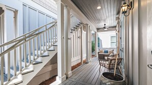 A covered porch with a wooden staircase, outdoor seating, and a potted plant. - Beach Bike Cottage 5 Bedroom, King Beds, Coastal Luxury Living, EV Charger (Seacrest Beach)