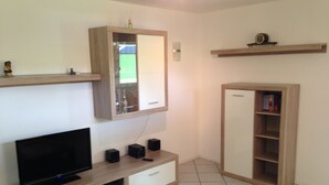 Ein Wohnzimmer mit Flachbildfernseher, Holzausbau, Couchtisch und Bücherregal.