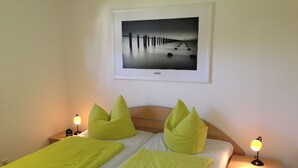 Ein ordentlich bezogenes Bett mit grüner Bettwäsche und Kissen, ein Nachttisch mit Lampe sowie ein gerahmtes Bild an der Wand.